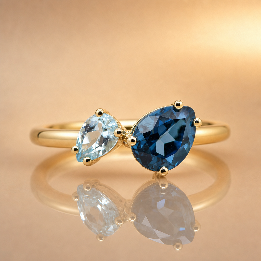 Gold ring with pear-shaped blue and clear gemstones on a reflective gold surface.